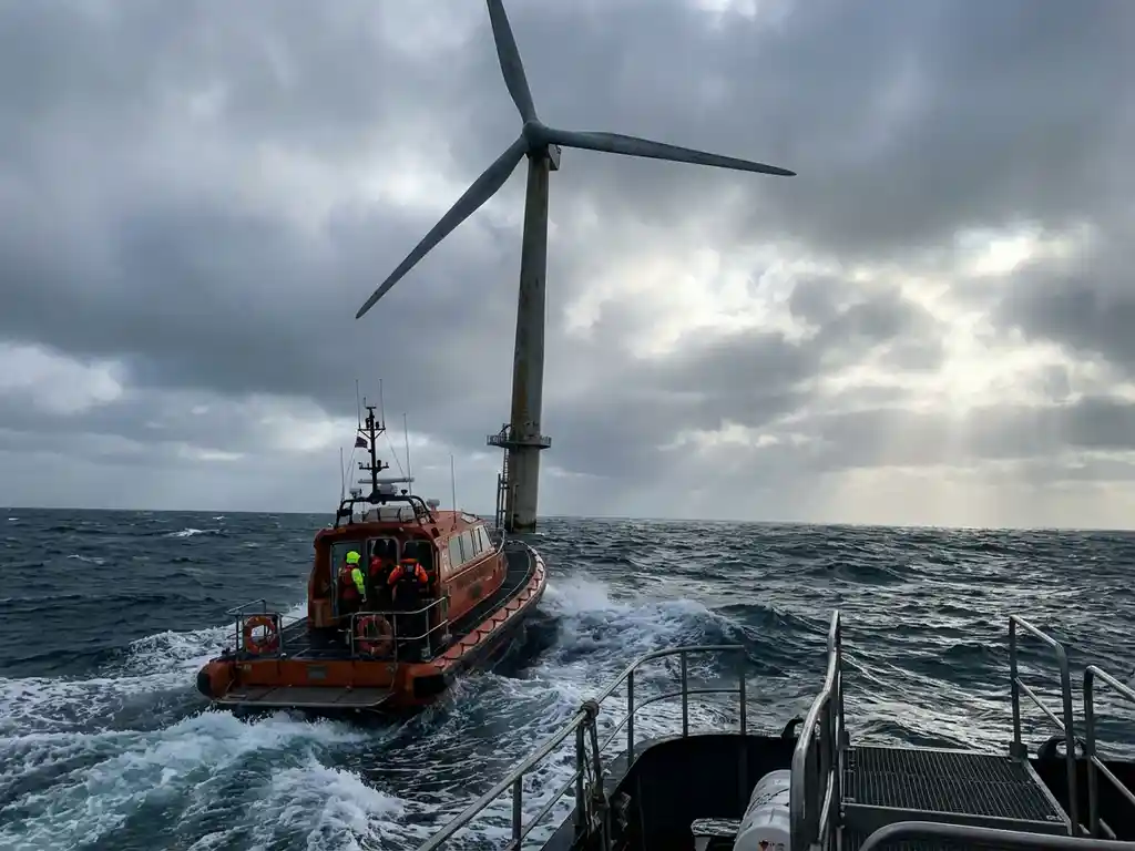 Offshore wind turbine rising from choppy ocean waters with storm clouds overhead and small inspection vessel battling waves